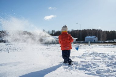 Banliyöde güneşli bir kış gününde kürekle kar atan bir çocuk..