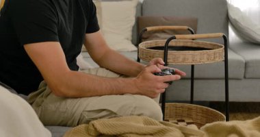 Evdeki kanepede video oyunu oynayan, elinde oyun kumandası olan, gündelik modern oturma odasında dinlenen bir adam..