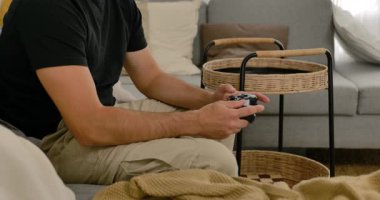 Evdeki kanepede video oyunu oynayan, elinde oyun kumandası olan, gündelik modern oturma odasında dinlenen bir adam..