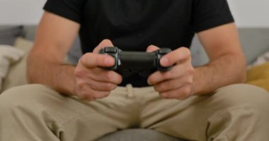 Evdeki kanepede video oyunu oynayan, elinde oyun kumandası olan, gündelik modern oturma odasında dinlenen bir adam..