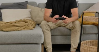 Evdeki kanepede video oyunu oynayan, elinde oyun kumandası olan, gündelik modern oturma odasında dinlenen bir adam..