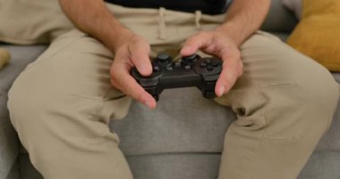 Evdeki kanepede video oyunu oynayan, elinde oyun kumandası olan, gündelik modern oturma odasında dinlenen bir adam..