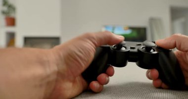 Modern oturma odasında video oyunu denetleyicisini tutan ellerin yakın çekimi, arka planda televizyon ekranı.