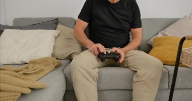 Evdeki kanepede video oyunu oynayan, elinde oyun kumandası olan, gündelik modern oturma odasında dinlenen bir adam..