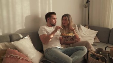 Bir çift sıcak oturma odasında patates kızartması ve tavuk nugget paylaşıyor..