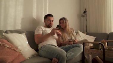 Çift, yakınlarda atıştırmalık eşliğinde akıllı telefonlar kullanarak koltukta dinleniyor..