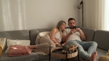 Çift, yakınlarda atıştırmalık eşliğinde akıllı telefonlar kullanarak koltukta dinleniyor..