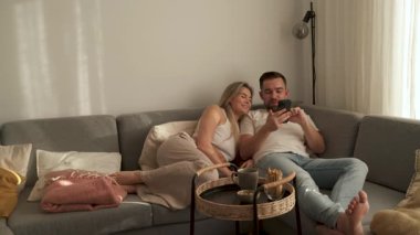 Çift, yakınlarda atıştırmalık eşliğinde akıllı telefonlar kullanarak koltukta dinleniyor..