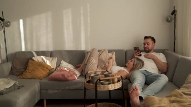 Çift, yakınlarda atıştırmalık eşliğinde akıllı telefonlar kullanarak koltukta dinleniyor..