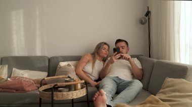 Çift, yakınlarda atıştırmalık eşliğinde akıllı telefonlar kullanarak koltukta dinleniyor..