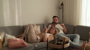 Çift, yakınlarda atıştırmalık eşliğinde akıllı telefonlar kullanarak koltukta dinleniyor..