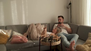 Çift, yakınlarda atıştırmalık eşliğinde akıllı telefonlar kullanarak koltukta dinleniyor..