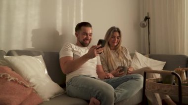 Çift, yakınlarda atıştırmalık eşliğinde akıllı telefonlar kullanarak koltukta dinleniyor..