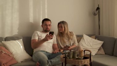 Çift, yakınlarda atıştırmalık eşliğinde akıllı telefonlar kullanarak koltukta dinleniyor..