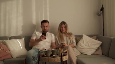 Çift, yakınlarda atıştırmalık eşliğinde akıllı telefonlar kullanarak koltukta dinleniyor..