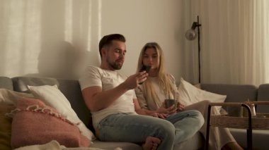 Çift, yakınlarda atıştırmalık eşliğinde akıllı telefonlar kullanarak koltukta dinleniyor..