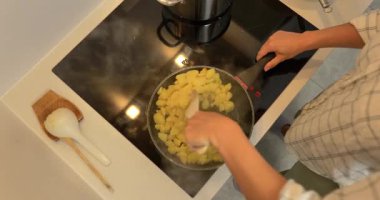 İndüksiyon ocağında haşlanmış patates parçalarını tavada kızartan ellerin yakın çekimi..