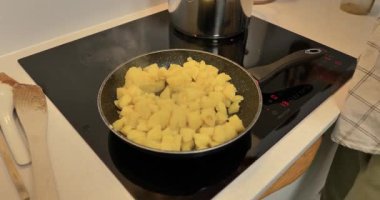 İndüksiyon ocağında haşlanmış patates parçalarını tavada kızartan ellerin yakın çekimi..