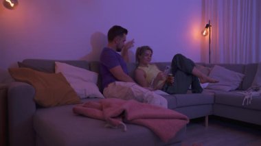 Evdeki rahat bir akşamda içki ve akıllı telefonla koltukta oturan çift..