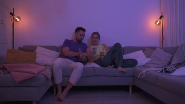 Evdeki rahat bir akşamda içki ve akıllı telefonla koltukta oturan çift..