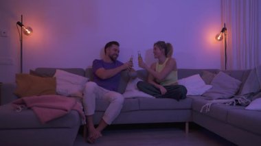 Çift kanepede oturuyor, sıcak bir oturma odasında bira ve nachos yiyor..