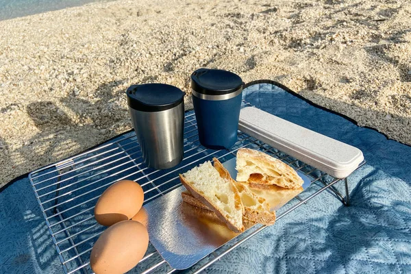 Travel food for outdoor activities. Two metal thermo cups, eggs and toast on a summer  background. Enjoy a tasty food during trips.