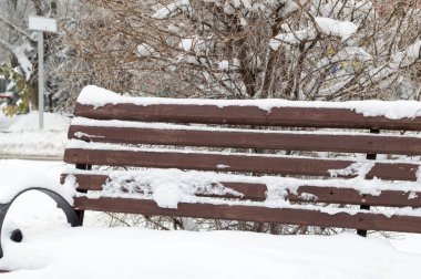 Tahta kahverengi kar kaplı bir bank sokakta duruyor.