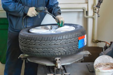 Mavi üniformalı tamirci lastik standında duran bir tekere hava pompalıyor.