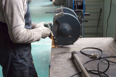 Gri tulumlu bir tamirci öğütme makinesinde metal bir parça işliyor.