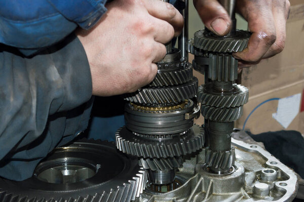 A blue-uniformed mechanic installs the primary and secondary shafts in the manual transmission housing