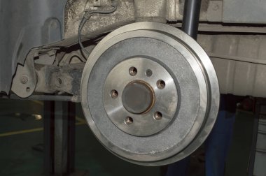 Bir araba tamirhanesinde asansörde asılı duran arabanın sol arka tekerine monte edilmiş bir fren davulu.