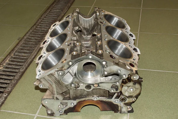 The cylinder block of a six-cylinder V-shaped internal combustion engine lies on the floor in an auto repair shop