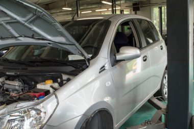 Kaputu açık gri bir araba bir araba tamirhanesinde gri bir asansöre monte edilir.