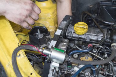 Bir tamirci, sarı bir arabaya dizel içten yanmalı motor takar.