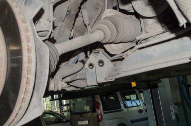 Otomobil tamirhanesindeki asansörde asılı duran arabanın sağ ön yarım dingilinin görüntüsü. Süspansiyon kısmen sökülmüş.