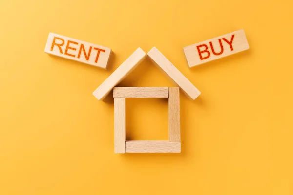 rent buy home. house made of wooden cubes with the words rent and buy on an orange background