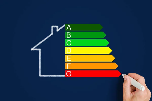 Ein Mann Zeichnet Ein Haus Neben Einer Energieeffizienzbewertung Auf Blauem lizenzfreie Stockfotos