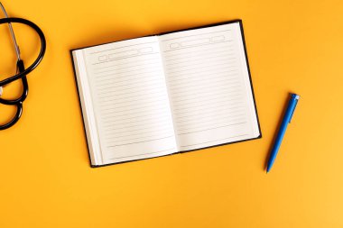 Boş not defteri, steteskop ve parlak turuncu arkaplanlı kalem.