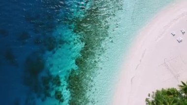 Tropik bir plajın kuş bakışı görüntüsü. Gün batımında mavi kumsalın en üst manzarası. Gün batımında beyaz kumlu güzel bir sahil. Tropikal bir sahilin kuş bakışı görüntüsü, deniz dalgaları güzel bir kıyı şeridinde düzgünce yuvarlanıyor..