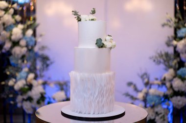 Çiçeklerle süslenmiş beyaz düğün pastası bir restoranda kemerin arka planına karşı