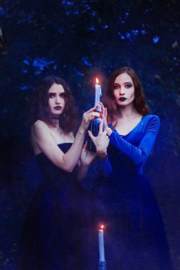 Cadılar Bayramı 'nda elinde mumla güzel kızlar. Mavi duman arka planı. Cadılar Bayramı için iki cadı..