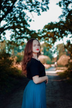 Güzel genç kız mavi pofuduk elbisesiyle bir yaz parkında yürüyor.