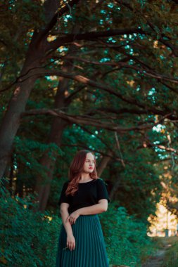 Peri ormanında turkuaz etekli bir kız. Kırmızı rujlu, gülümseyen tatlı kız. Büyük ağaç dallarının arka planındaki kız