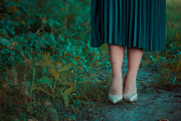 Beautiful female legs in beige shoes on the background of nature. Turquoise skirt. Femininity. Place for text