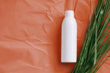 Cilt ürünlerinin maketi için plastik boş etiket şişesi. Doğal güzellik ürünü konsepti. Turuncu arka planda yeşil yapraklı kozmetik kompozisyonu