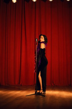 Akşam şovu sırasında kırmızı perdenin önünde mikrofonla sahnede zarif bir sanatçı.