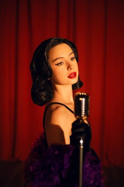 Sahnede zarif bir şekilde şarkı söyleyen bir kadın mikrofonla kırmızı perde arkasından şarkı söylüyor.