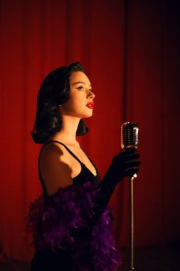 Sahnede zarif bir şekilde şarkı söyleyen bir kadın mikrofonla kırmızı perde arkasından şarkı söylüyor.