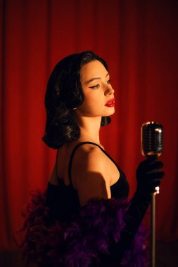 Sahnede zarif bir şekilde şarkı söyleyen bir kadın mikrofonla kırmızı perde arkasından şarkı söylüyor.