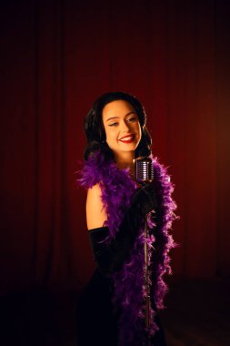 Sahnede zarif bir şekilde şarkı söyleyen bir kadın mikrofonla kırmızı perde arkasından şarkı söylüyor.